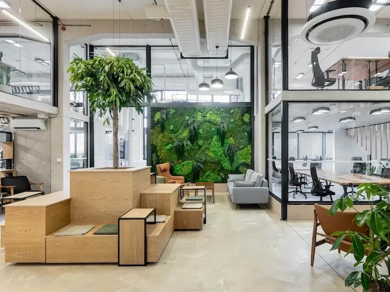 The Puzl CoWorking common area in Budapest — wooden seating, a living moss wall, and glass-walled offices.